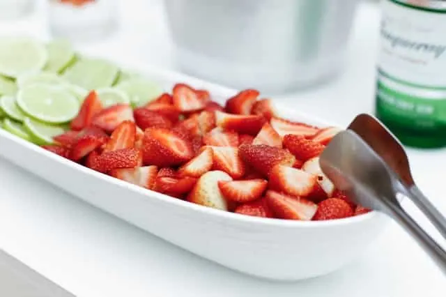 Fresas troceadas en una fuente blanca alargada junto a rodajas de lima