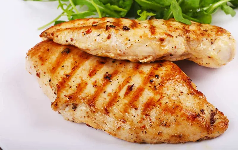Pechugas de pollo a la plancha con marcas de parrilla, servidas con hojas verdes