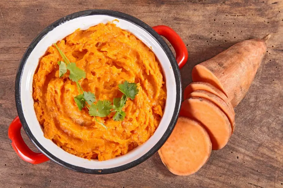 Puré de batata cremoso en una cazuela roja, junto a rodajas de batata cruda