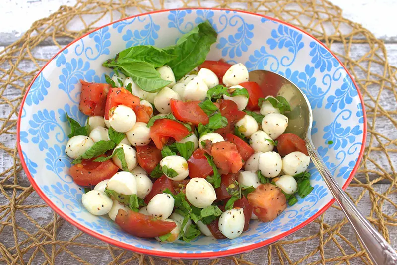 Ensalada capresa con bolitas de mozzarella, tomate y albahaca en un bol de cerámica