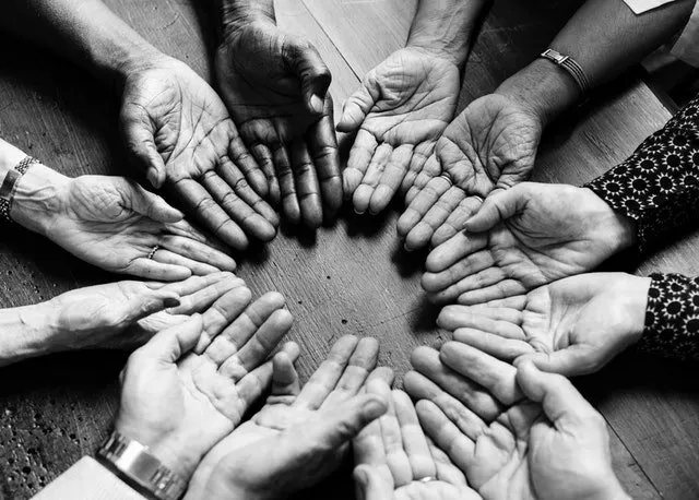 Manos de varias personas abiertas y unidas formando un círculo, en blanco y negro