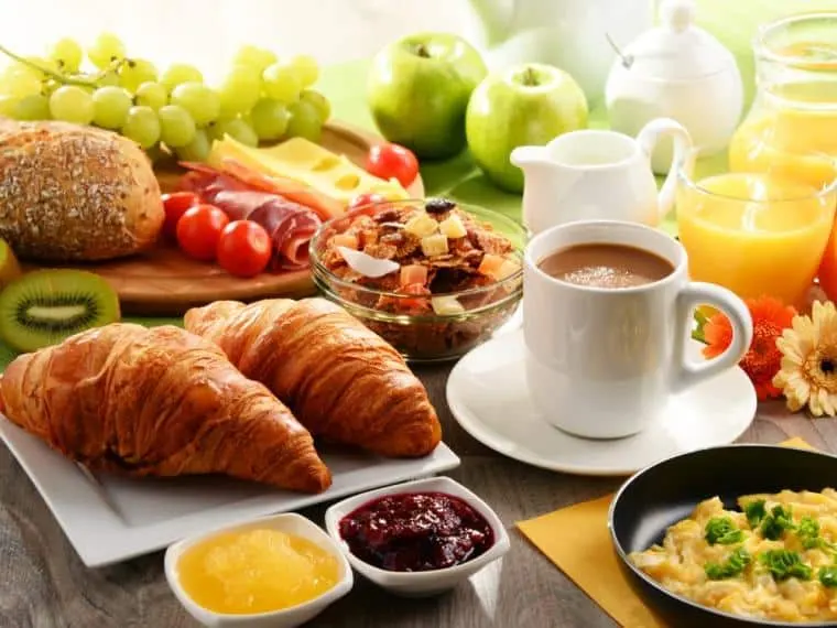 Mesa de desayuno con bollería, pan, frutas, café y zumo de naranja