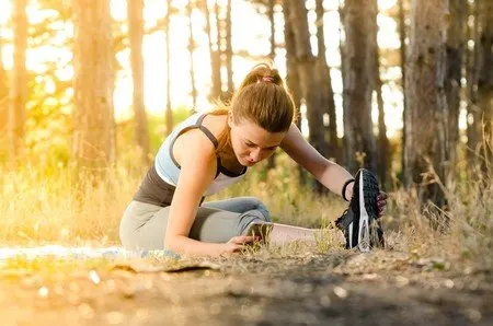 Mujer atándose la zapatilla y estirando en un camino de bosque en otoño