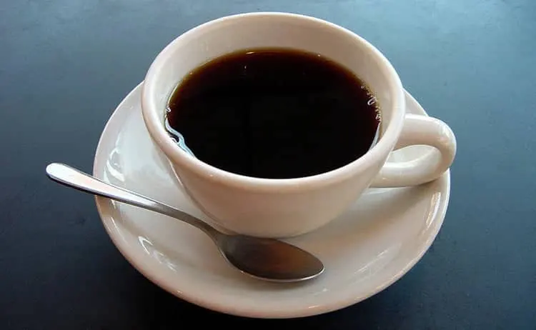 Taza de café negro recién servido sobre un platillo con cuchara