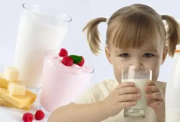 Niña bebiendo un vaso de leche junto a queso, yogur y un batido de fresa