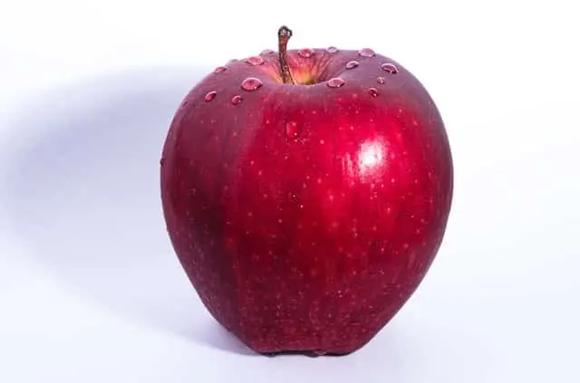 Manzana roja con gotas de agua sobre un plato blanco