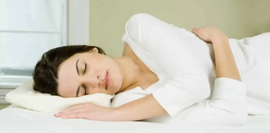Mujer durmiendo de lado en una cama con ropa de cama blanca