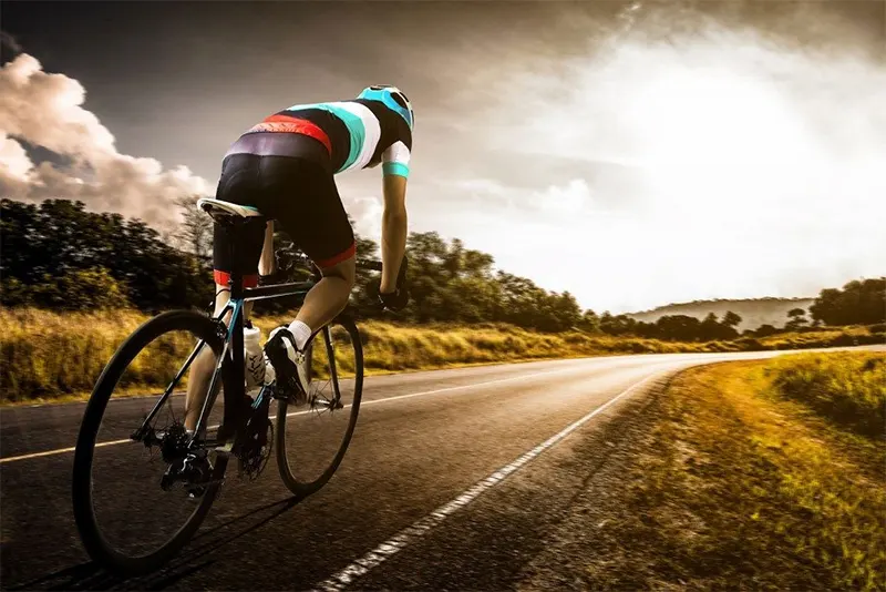 Ciclista de carretera pedaleando inclinado sobre la bicicleta al atardecer