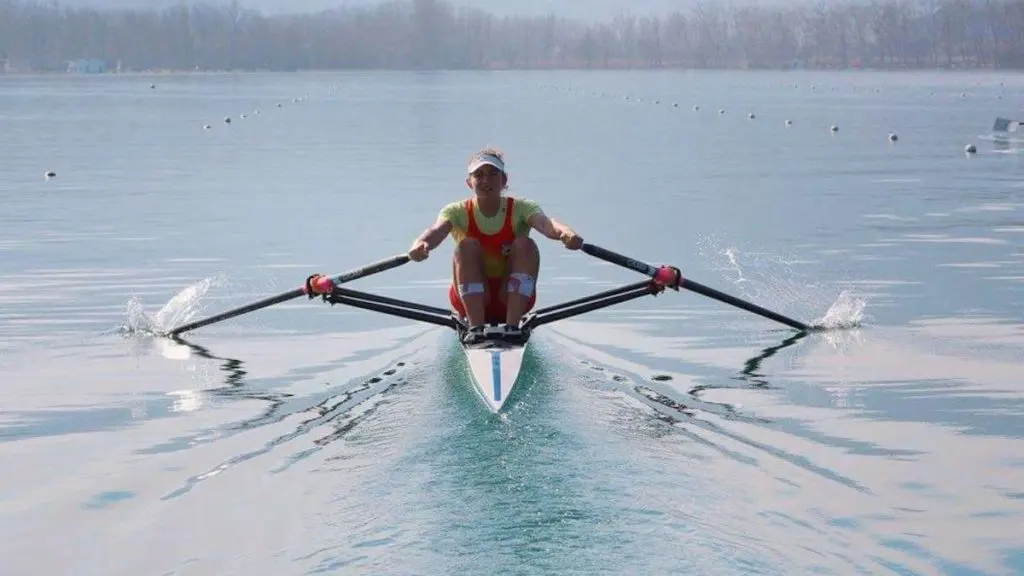 Remero avanzando en un bote individual sobre un lago en calma