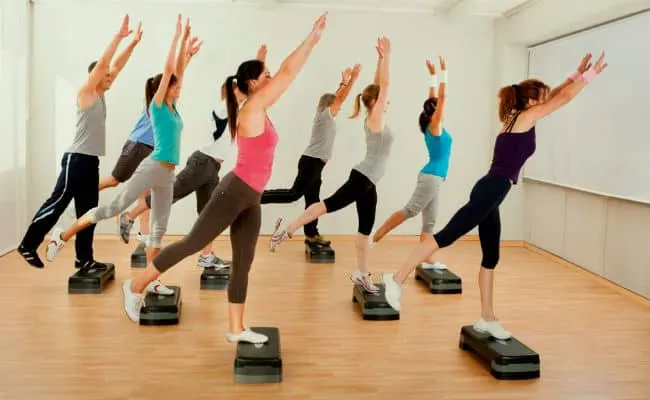 Clase de step con los brazos levantados sobre plataformas de aeróbic