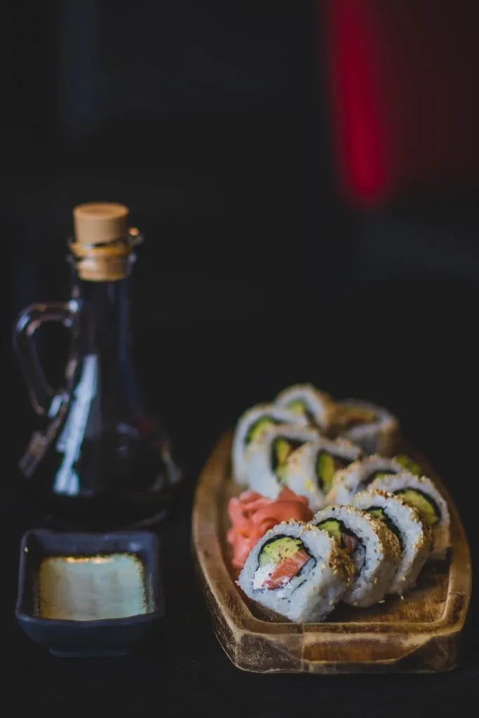 Bandeja de sushi variado junto a una botella de salsa sobre fondo oscuro