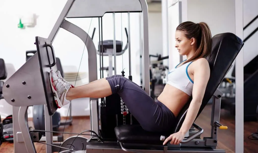 Mujer empujando la plataforma de una prensa de piernas en el gimnasio