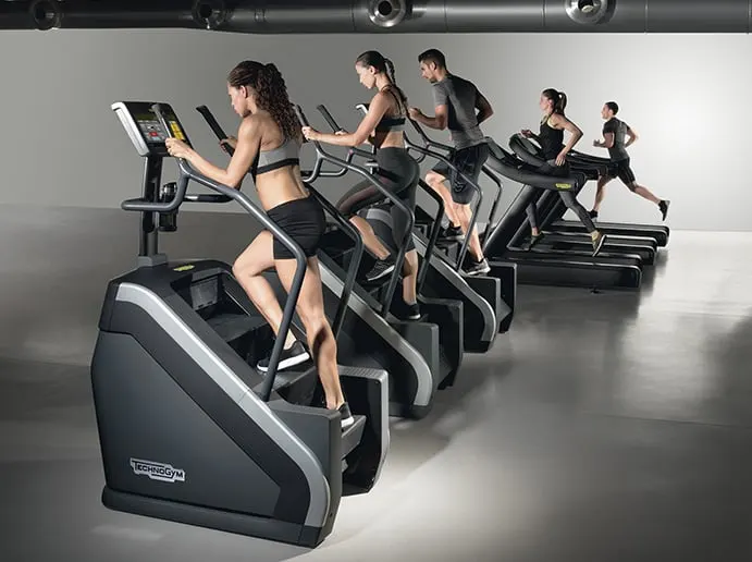 Fila de escaladoras y cintas de correr con personas entrenando en un gimnasio