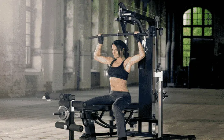 Mujer sentada haciendo jalón al pecho en una máquina multiestación