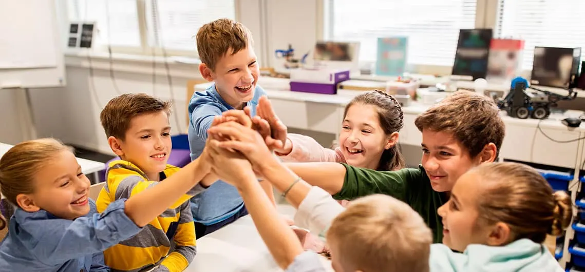 Grupo de niños juntando las manos en el centro de un aula
