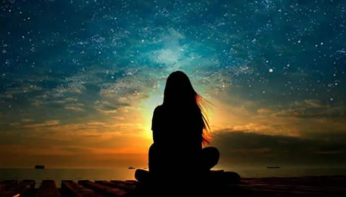 Silueta de una persona meditando sentada frente a un cielo estrellado al atardecer