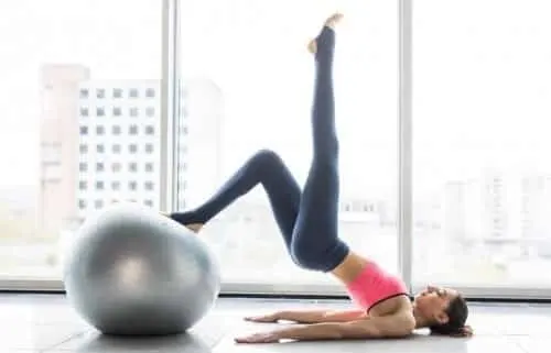 Mujer haciendo un ejercicio de pilates apoyada en una pelota junto a un ventanal