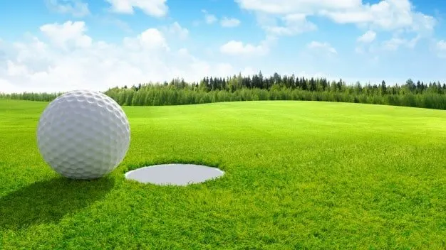 Pelota de golf junto al hoyo en un green de césped