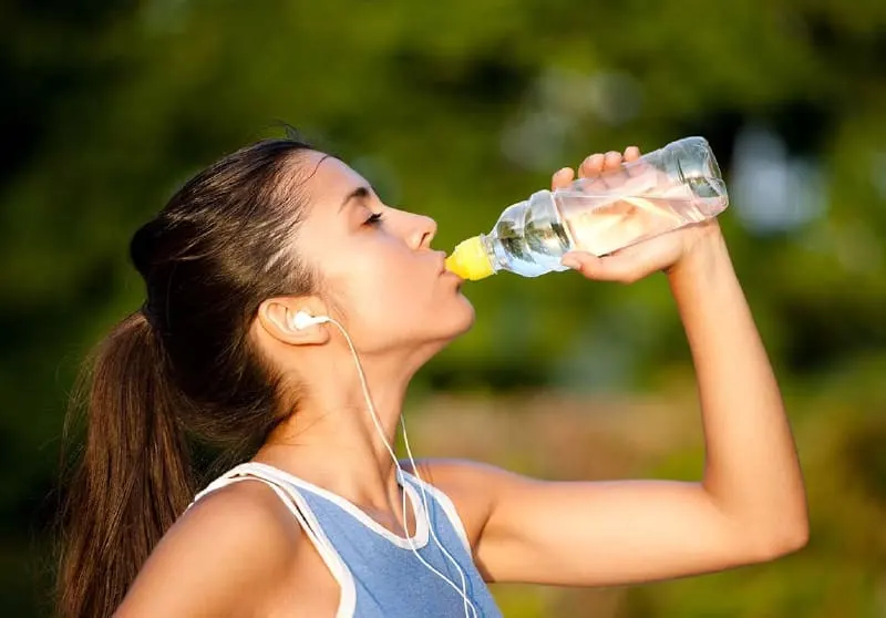 Mujer bebiendo agua de una botella después de entrenar al aire libre