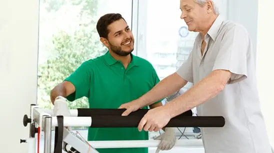 Paciente mayor trabajando con un aparato de rehabilitación asistido por un terapeuta