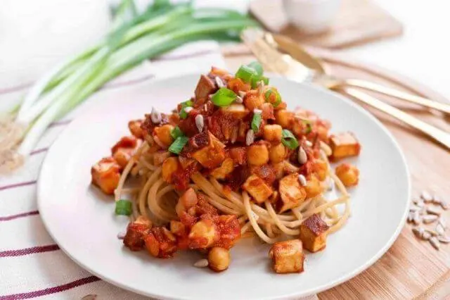 Espaguetis con salsa de tomate y tofu salteado, servidos en un plato blanco