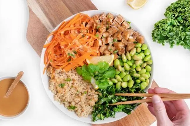 Bol de arroz integral con zanahoria, edamame y kale, comido con palillos