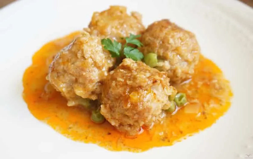 Albóndigas en salsa de tomate con guisantes, servidas en un plato hondo