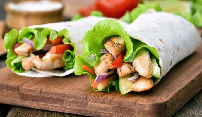 Wrap de pollo con lechuga y verduras, cortado sobre una tabla de madera