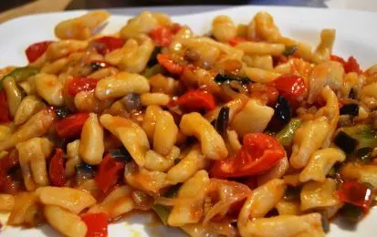 Pasta corta salteada con pimientos y tomate en un plato blanco