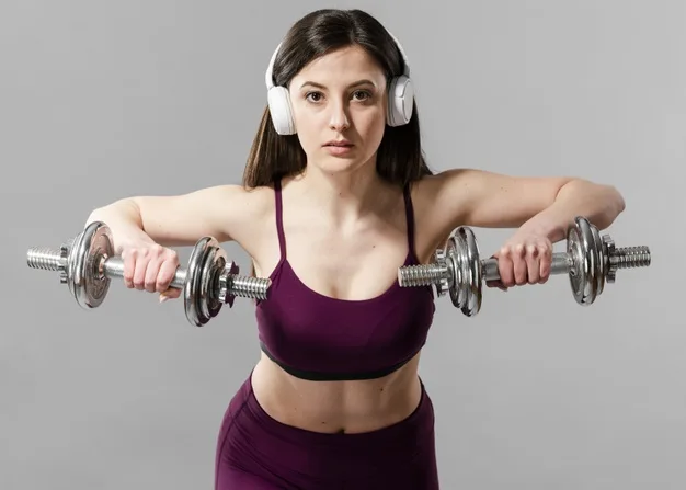 Mujer con auriculares sosteniendo dos mancuernas cruzadas a la altura del pecho