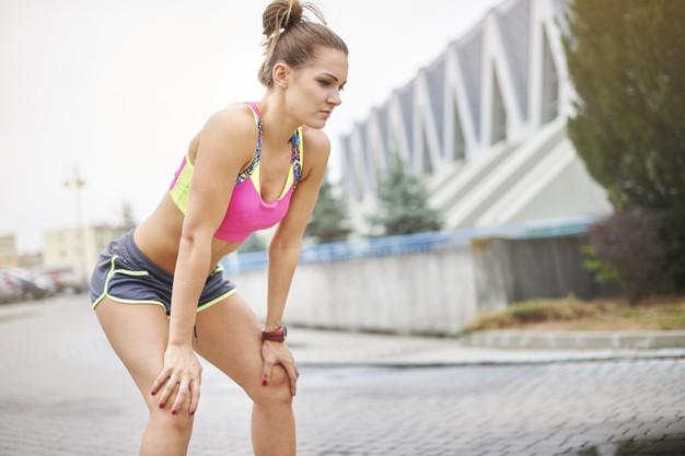 Mujer apoyada en las rodillas recuperando el aliento después de entrenar en la calle